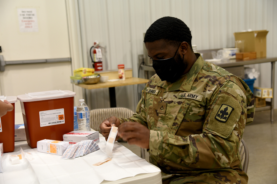 Private 1st Class Theron Johnson, 1-158th Infantry Battalion, combat medic, prepares bandages to be used after administering COVID-19 vaccinations