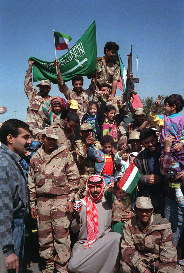 Civilians and coalition military forces wave Kuwaiti and Saudi Arabian flags