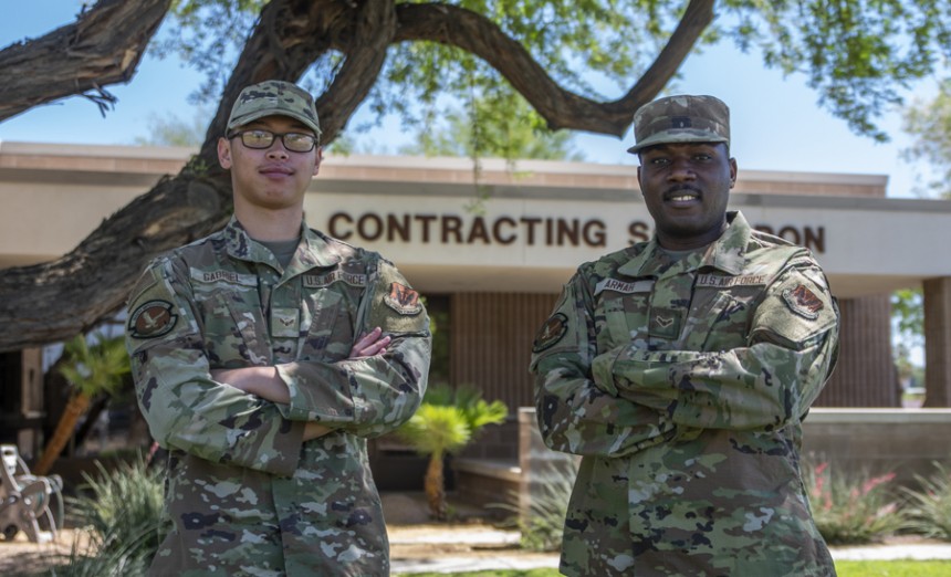 Airman 1st Class Hans Gabriel, left, and Airman 1st Class Eric Armah, both 355th Contracting Squadron contracting specialists, stand in front of the contracting squadron at Davis-Monthan Air Force Base, Ariz., May 25, 2022. Both Airmen enlisted in the U.S. Air Force to provide for their families. (Air Force photograph by Staff Sgt. Kristine Legate)
