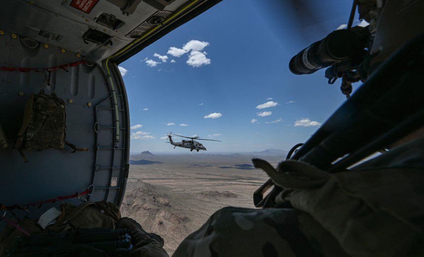A U.S. Air Force Airman watches an HH-60W Jolly Green II helicopter, assigned to Kirtland Air Force Base, N.M., fly during Red Flag-Rescue 23-1 over Arizona, May 13, 2023. During this iteration of RF-R, Airmen from across the country, as well as Marines, Soldiers and Sailors worked together to complete multiple training exercises and build joint force relationships.