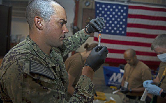 Navy photograph by PO1 Jacob Sippel Navy Petty Officer 3rd Class Bryan Reed, assigned to Michaud Expeditionary Medical Facility, prepares supplies for COVID-19 vaccines.