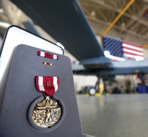 Air Force photograph by Senior Airman James Thompson A U.S. Air Force medal with an attached remote “R” device sits in front of an MQ-9 Reaper July 9, 2018, at Creech Air Force Base, Nev. The “R” device distinguishes an award earned for hands-on employment of a weapon system that had direct and immediate impact on a military operation, without being exposed to hostile action or immediate danger.