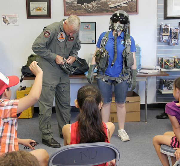 Photograph by Linda KC Reynolds Stephanie Cregier, director of the Junior Test Pilot School Summer Museum Program, dons flight gear with a little help from B-2 Test Pilot Don Weiss. Weiss also showed students what pilots must wear in order to be safe at high altitudes and how to survive when ejecting from an aircraft and landing in water.