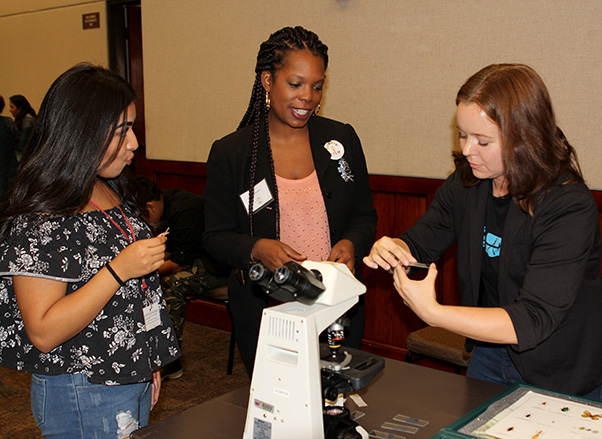 Photograph by Linda KC Reynolds Getting cheeky: Jazmin Sanchez from Highland High School and Mera Burton from Aero Institute hand their cheek cells to Antelope Valley College student Sarah Schroeder during The Antelope Valley East Kern STEM Network 5th annual STEMposium “The Future of Innovation.” The event helps school and industry leaders network to promote STEM education and learn what industries need from future employees.