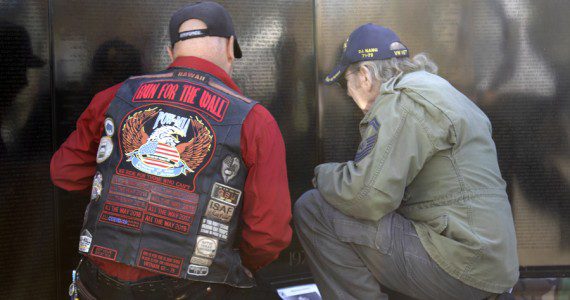 Two veterans kneel at the AV Wall mobile Vietnam Veterans mobile wall during the Veterans Day ceremony, Nov. 11, 2022. (Photograph by Adrienne King)