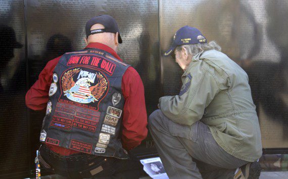 Two veterans kneel at the AV Wall mobile Vietnam Veterans mobile wall during the Veterans Day ceremony, Nov. 11, 2022. (Photograph by Adrienne King)