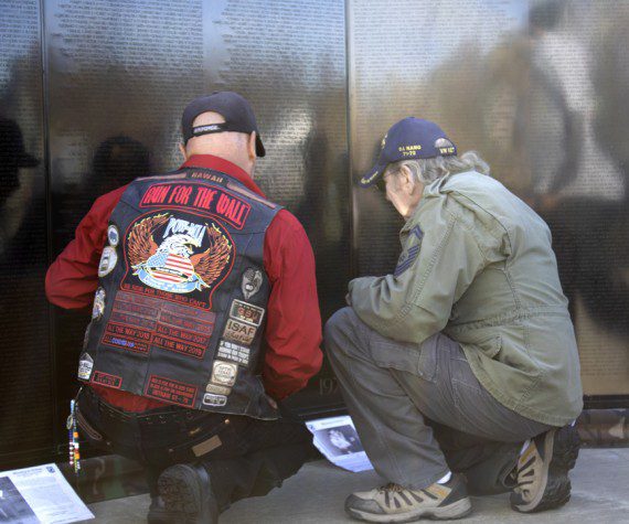 Two veterans kneel at the AV Wall mobile Vietnam Veterans mobile wall during the Veterans Day ceremony, Nov. 11, 2022. (Photograph by Adrienne King)