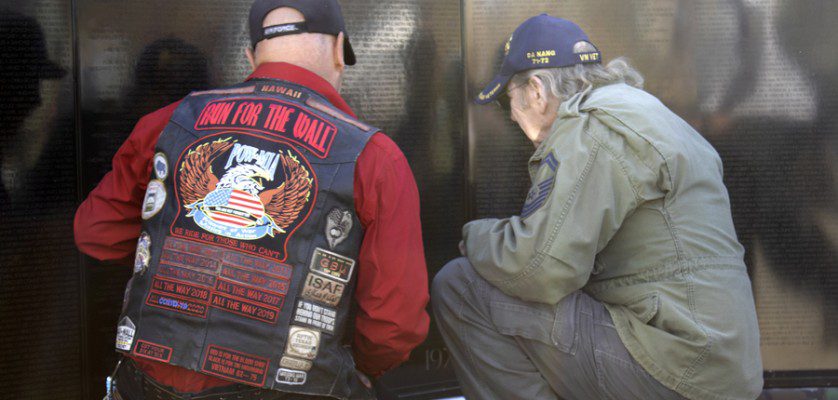 Two veterans kneel at the AV Wall mobile Vietnam Veterans mobile wall during the Veterans Day ceremony, Nov. 11, 2022. (Photograph by Adrienne King)