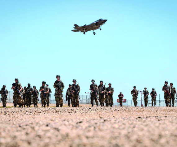 U.S. Air Force Airmen attending the John J. Rhoades Airman Leadership School march to a forward operating point near the flightline as an F-35A Lightning II prepares to land, May 2, 2025, at Luke Air Force Base, Arizona. Ready Airman Training, a day of hands-on training in which all ALS students participated, included tactical combat casualty care, runway repair, and clearing buildings. The students, drawn from various career fields, are preparing to become future non-commissioned officers in the Air Force. (U.S. Air Force photos by Airman 1st Class Belinda Guachun-Chichay)